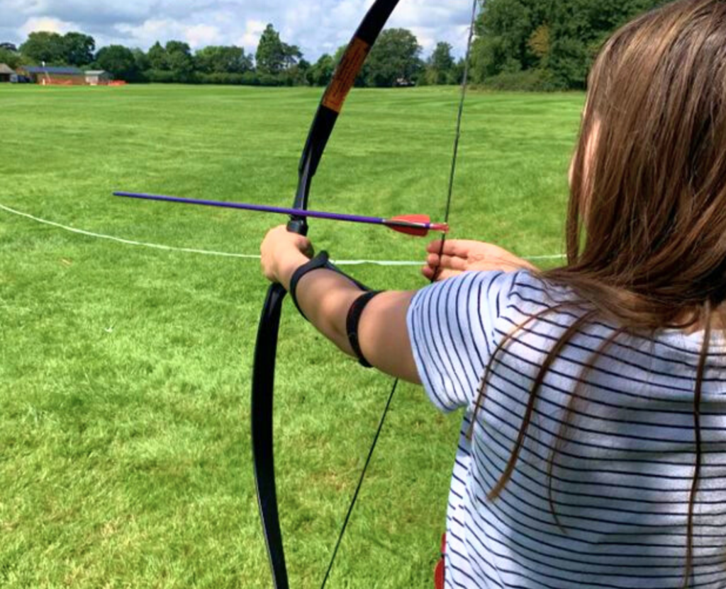 a girl learning how to shoot a bow and arrow